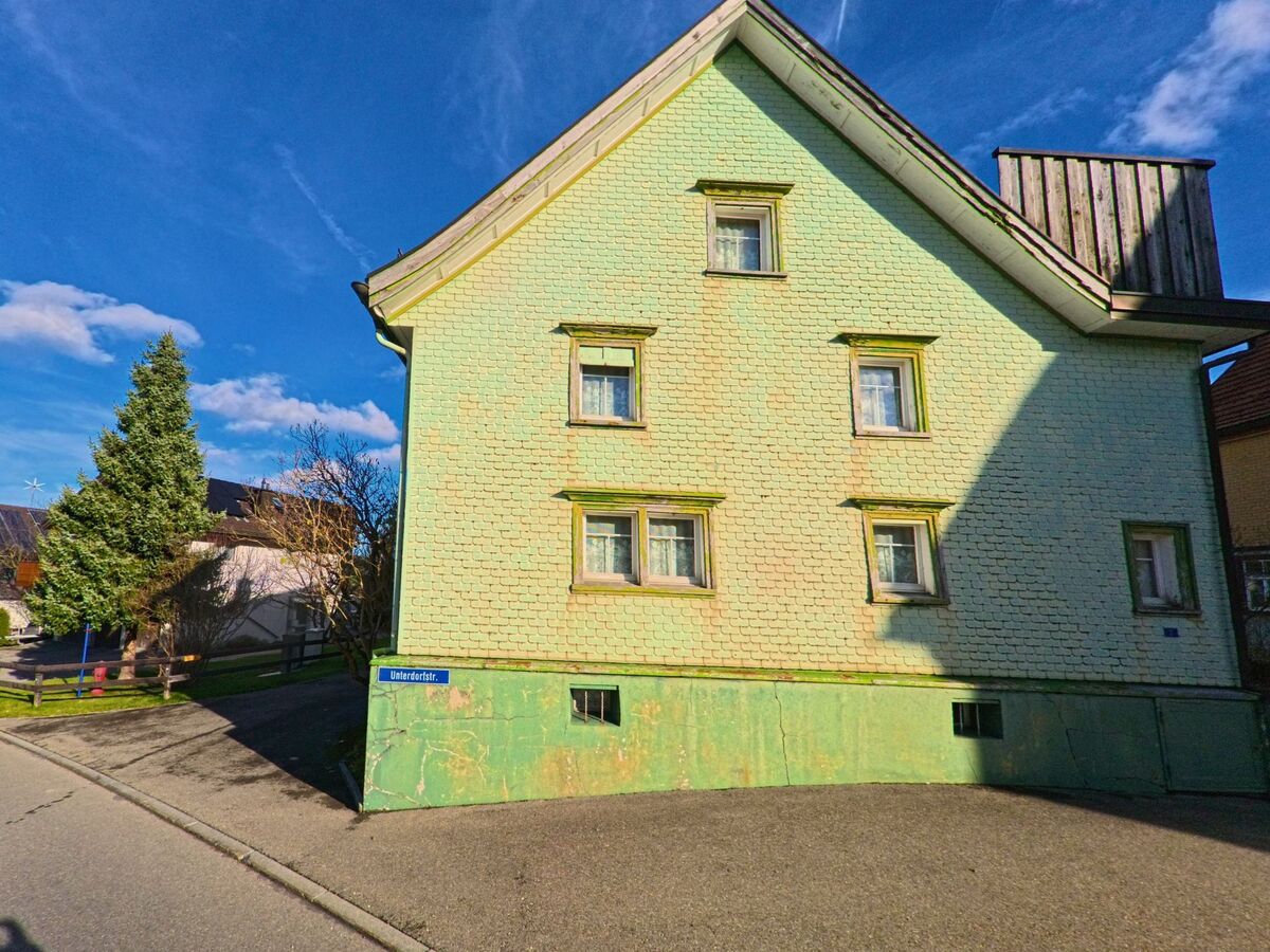 Ein hellgrün gestrichenes Wohngebäude steht an einer ruhigen Strasse in Oberegg (9413, Kanton Appenzell Innerrhoden) bei klarem Himmel.