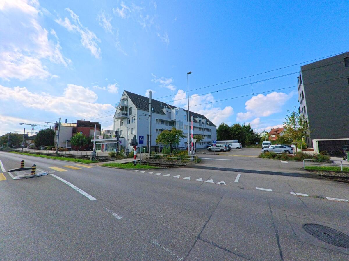 Moderne Mehrfamilienhaeuser und ein Bahnuebergang praegen das Strassenbild in Oberentfelden (5036, Kanton Aargau) bei sonnigem Wetter.