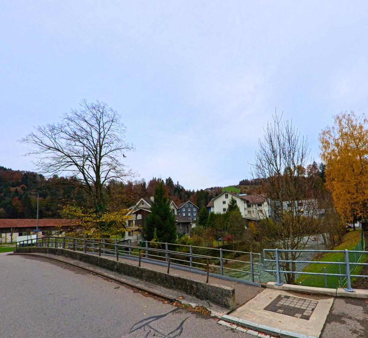 Eine kleine Bruecke fuehrt ueber einen Bach am Rand von Oberhelfenschwil (9125, Kanton St. Gallen) mit Blick auf Wohnhaeuser.