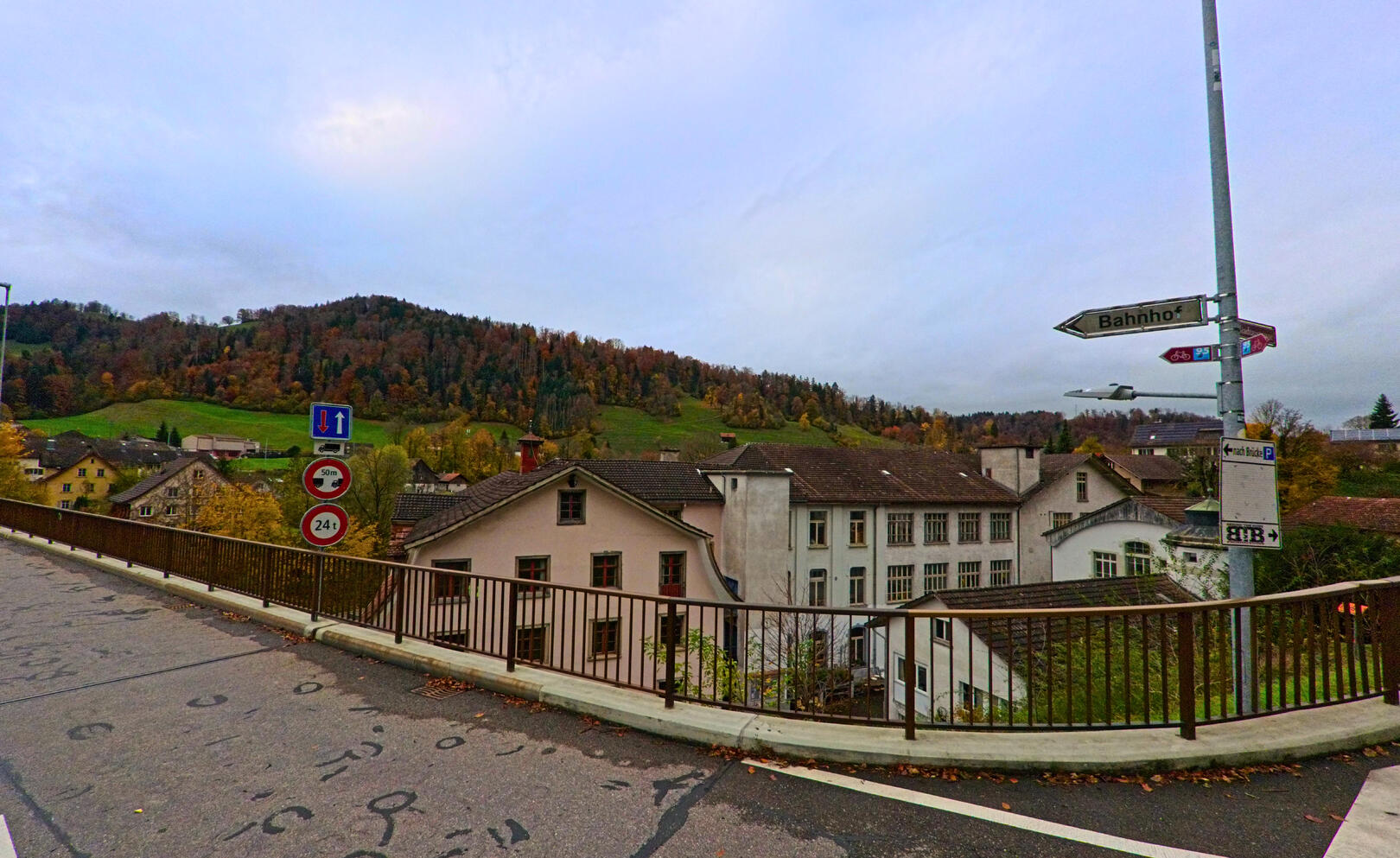 Von einer Bruecke aus zeigt sich der Blick auf Gebaeude und bewaldete Huegel in Oberhelfenschwil (9125, Kanton St. Gallen) unter herbstlichem Himmel.