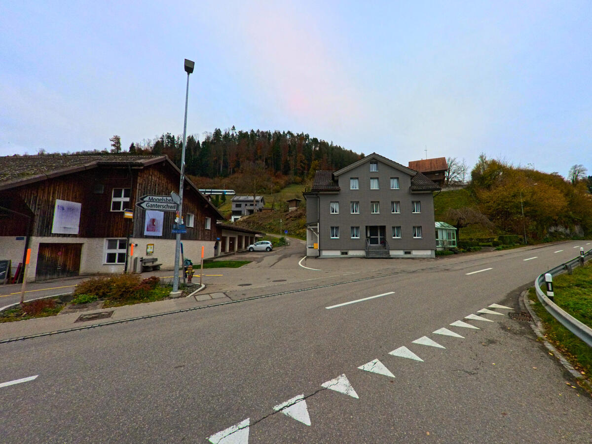 An einer Strassenkreuzung mit Markierungen stehen mehrere Gebaeude im Dorfzentrum von Oberhelfenschwil (9125, Kanton St. Gallen).