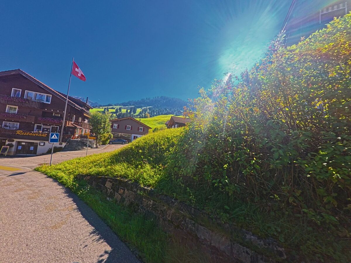 Bei sonnigem Wetter verläuft ein schmaler Weg entlang von Wiesen und Häusern in Oberiberg (8843, Kanton Schwyz).
