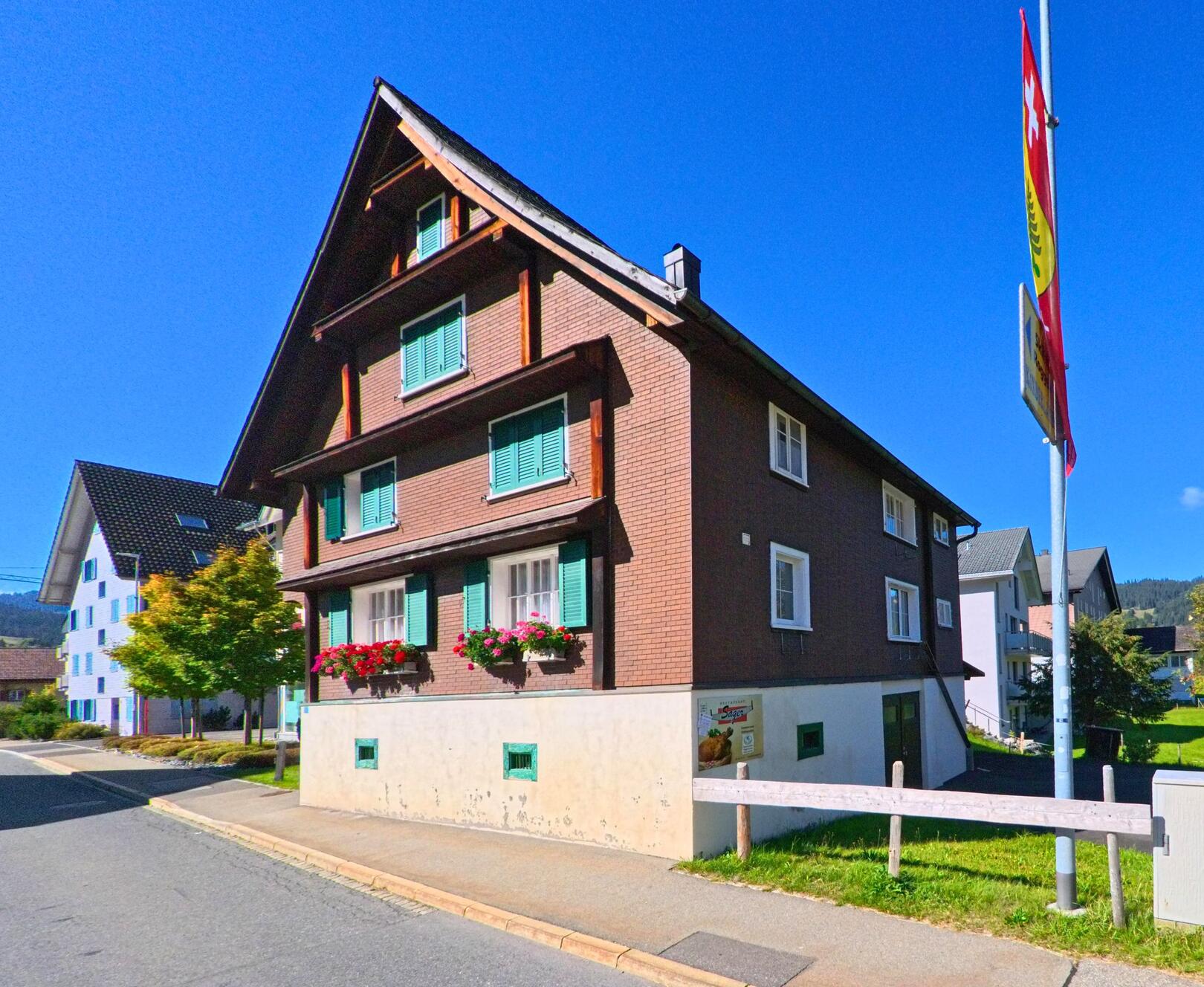 Ein traditionelles Haus in Oberiberg (8843, Kanton Schwyz) mit grünen Fensterläden und Blumenkästen, das sich harmonisch in die Umgebung einfügt.