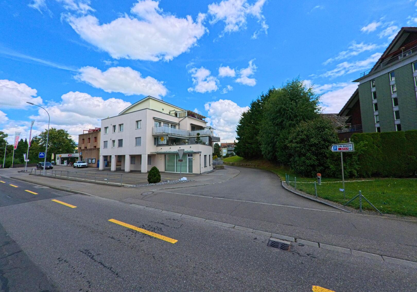 In Oberkirch (6208, Kanton Luzern) zweigt ein schmaler Seitenweg neben einem modernen Wohn- und Geschäftshaus von der Hauptstrasse ab.