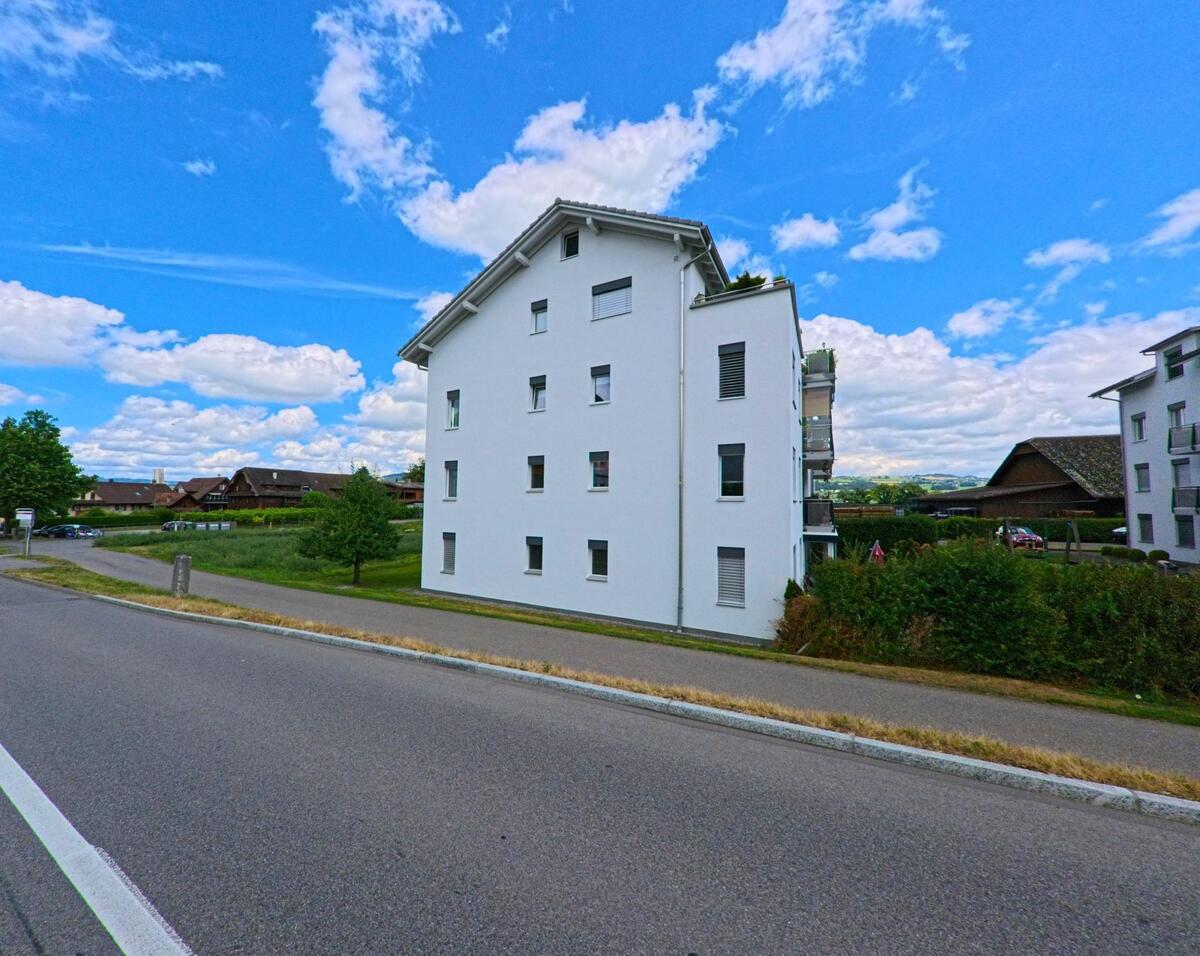 In Oberkirch (6208, Kanton Luzern) steht ein weiss verputztes Mehrfamilienhaus am Rand eines Wohngebiets mit Blick auf traditionelle Bauernhoefe.