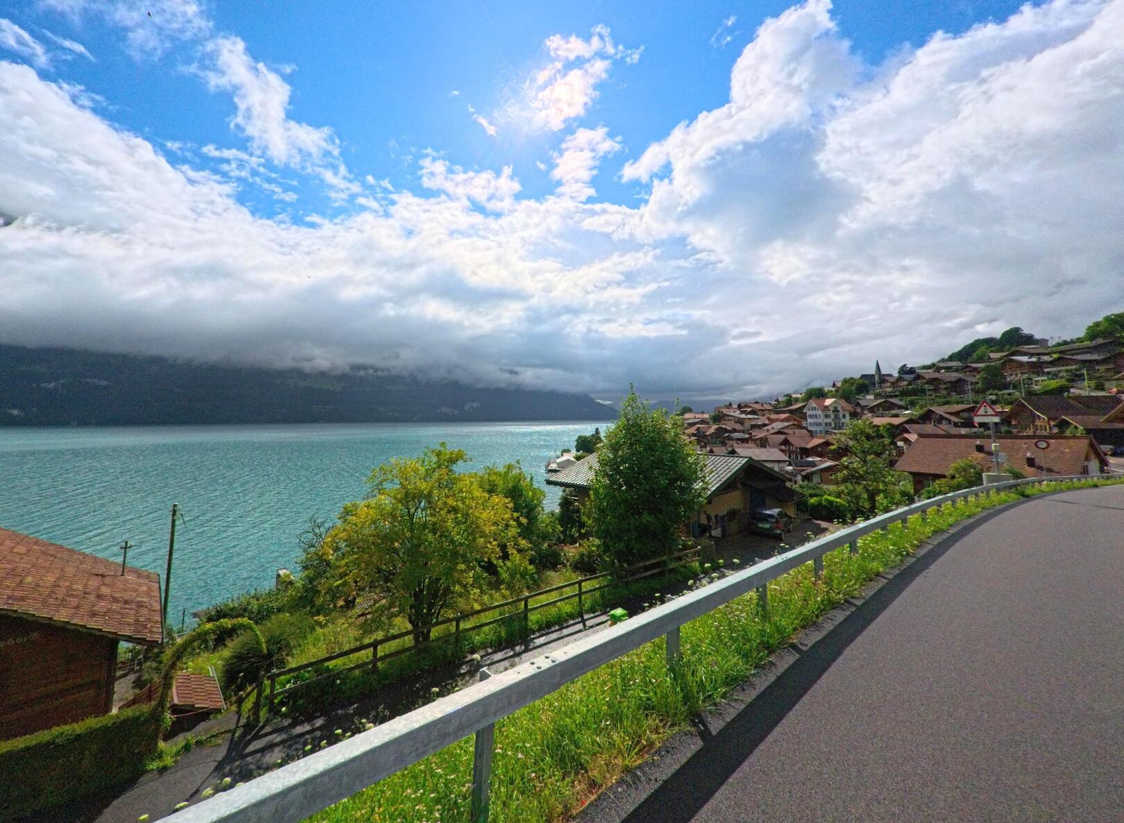 In Oberried am Brienzersee (3854, Kanton Bern) öffnet sich von einer Höhenstrasse der Blick über das Dorf und den türkisfarbenen See bis zu den bewölkten Berghängen.