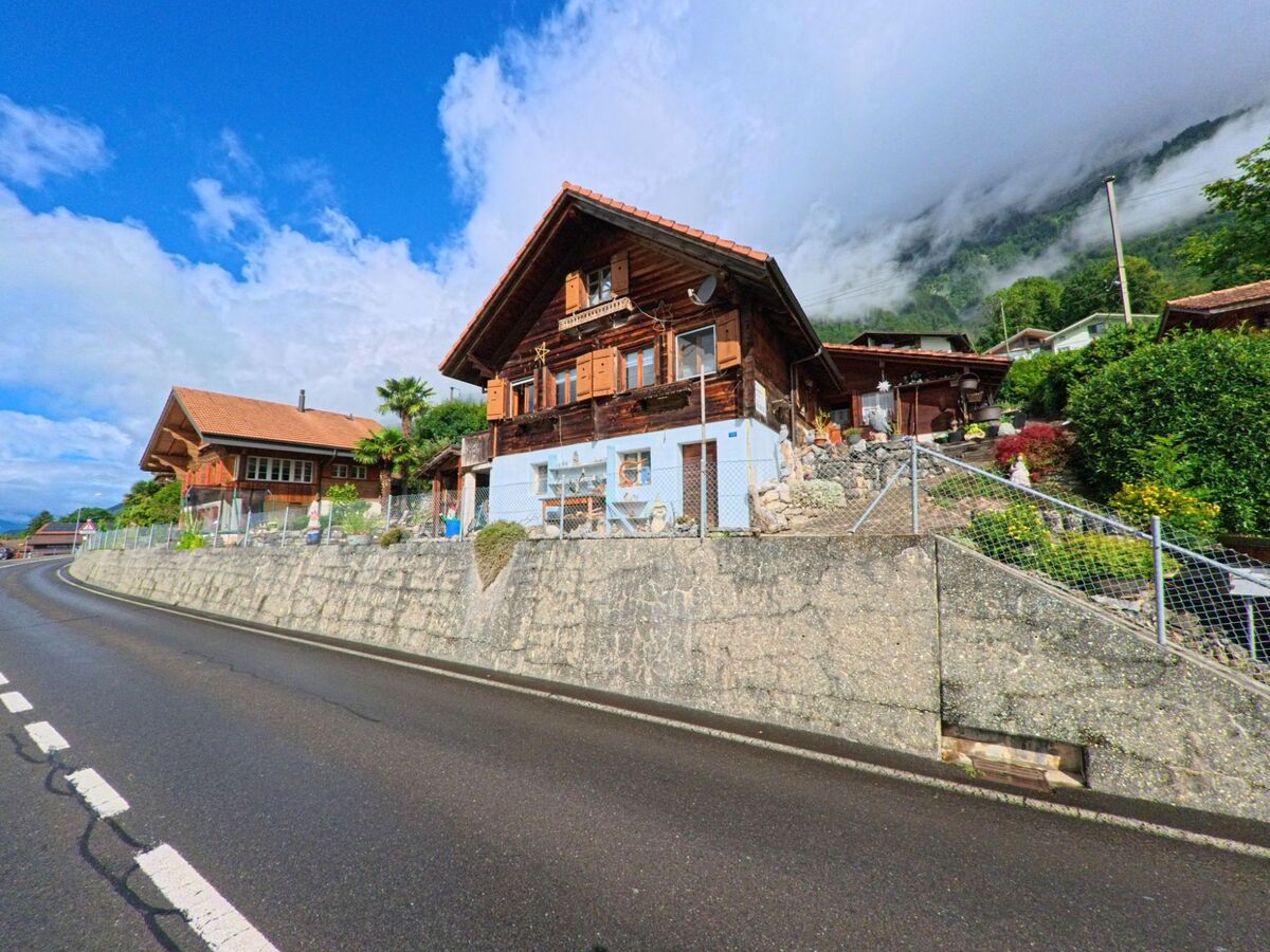 In Oberried am Brienzersee (3854, Kanton Bern) stehen gepflegte Holzhäuser mit kleinen Vorgärten an einer ansteigenden Strasse mit Blick auf den Hang.