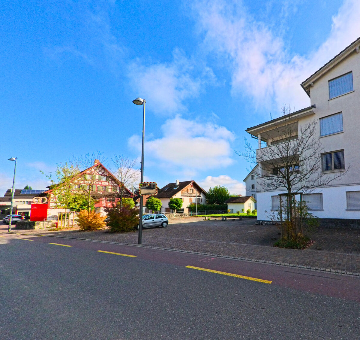 Eine ruhige Quartierstrasse mit Wohnhaeusern erstreckt sich durch Oberriet (9463, Kanton St. Gallen) bei klarem Himmel.