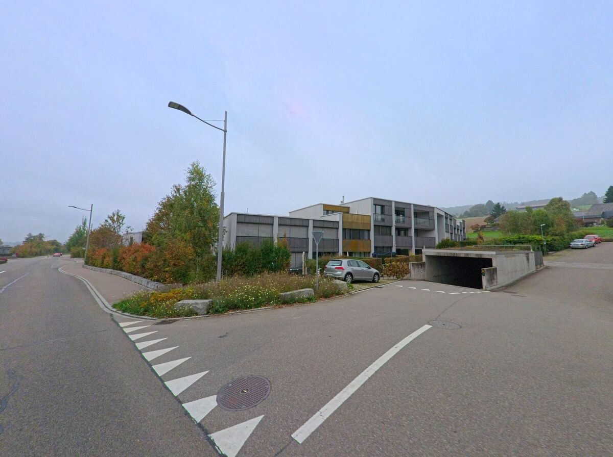 Moderne Mehrfamilienhaeuser mit Tiefgarageneinfahrt liegen in Oberrohrdorf (5452, Kanton Aargau) entlang einer leicht ansteigenden Strasse.