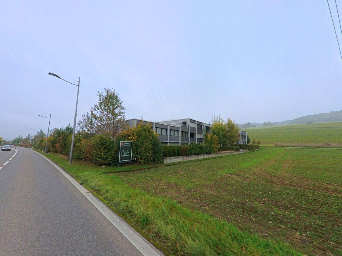 Am Ortsrand von Oberrohrdorf (5452, Kanton Aargau) liegen moderne Wohnbauten neben Feldern und sanft ansteigenden Huegeln.