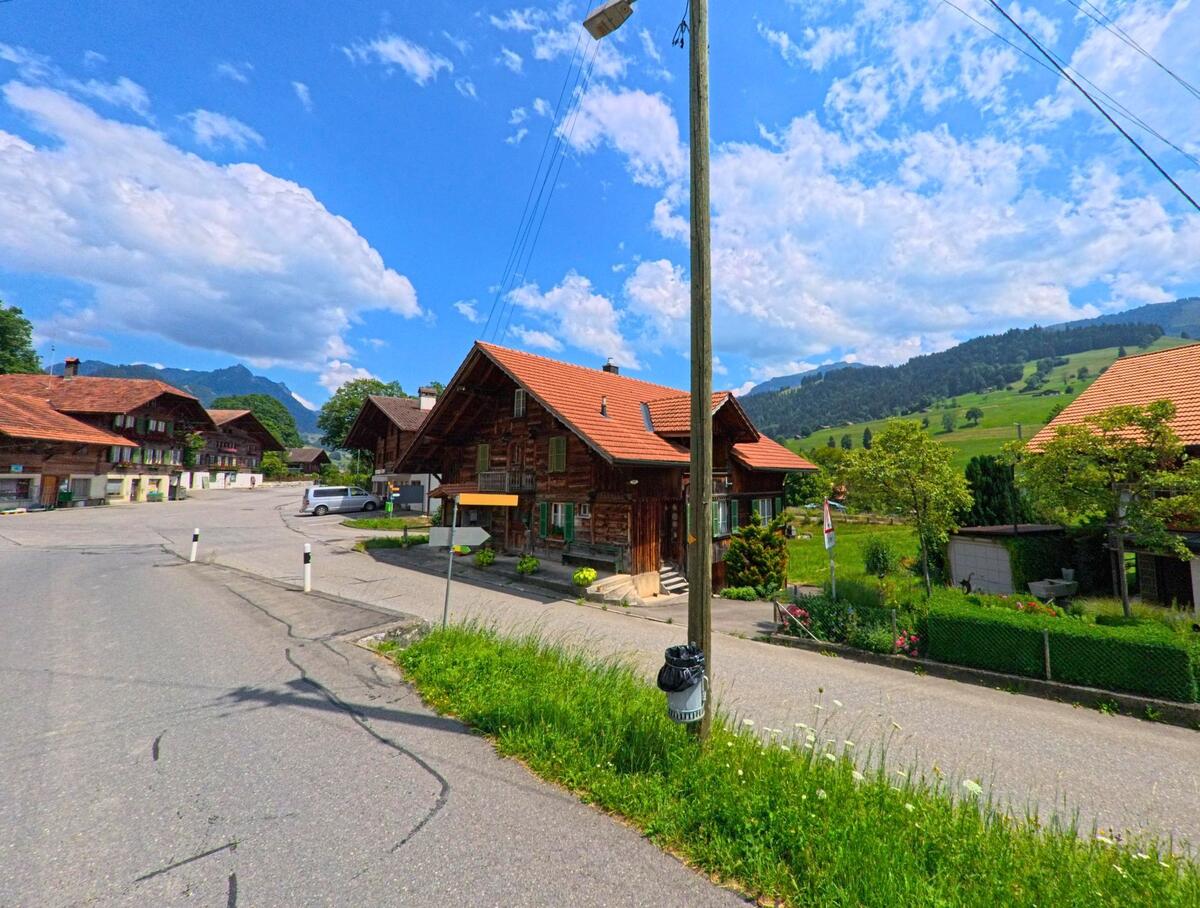 Im Dorfkern von Oberwil im Simmental (3765, Kanton Bern) reihen sich Holzhäuser mit roten Ziegeldächern entlang der Strasse mit Blick auf die umliegenden Hügel.