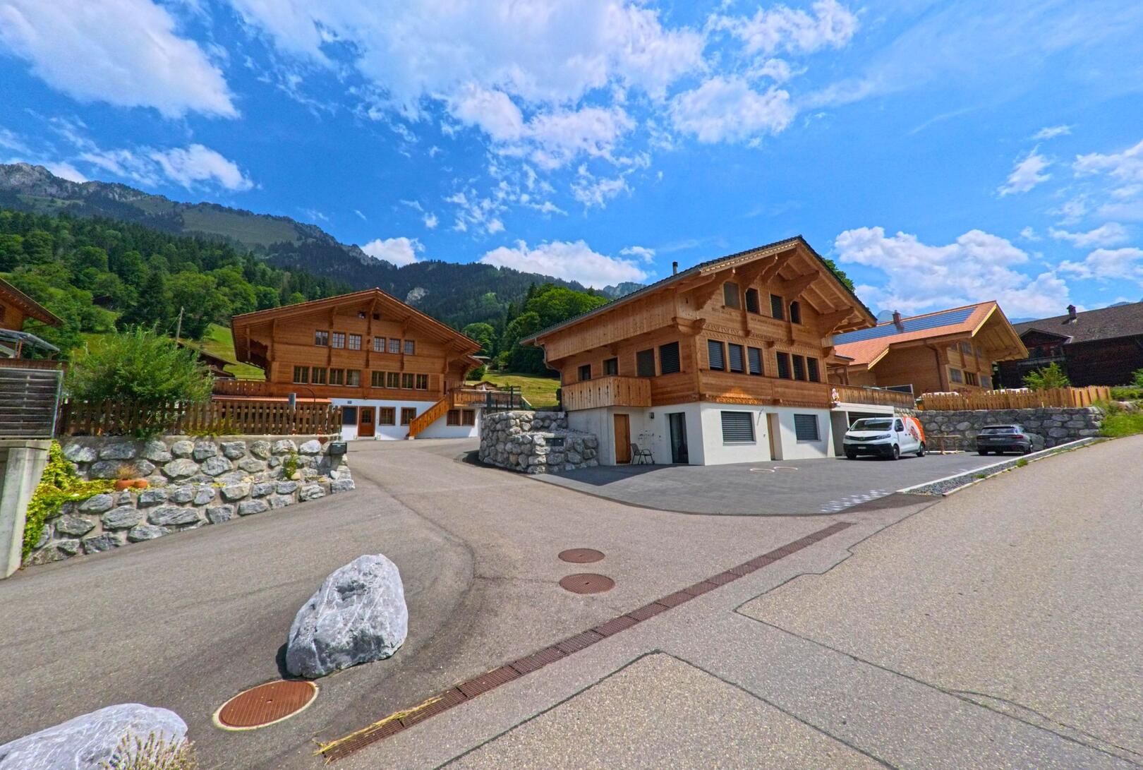 In Oberwil im Simmental (3765, Kanton Bern) stehen moderne Chalets aus hellem Holz an einem Hang mit Blick auf die bewaldeten Berghänge.