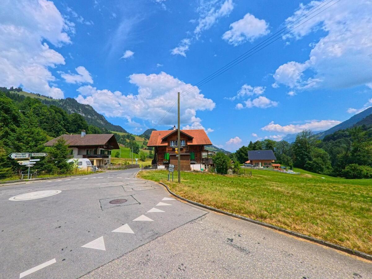 Am Ortseingang von Oberwil im Simmental (3765, Kanton Bern) treffen sich mehrere Strassen vor einem Wohnhaus inmitten grüner Hügellandschaft.