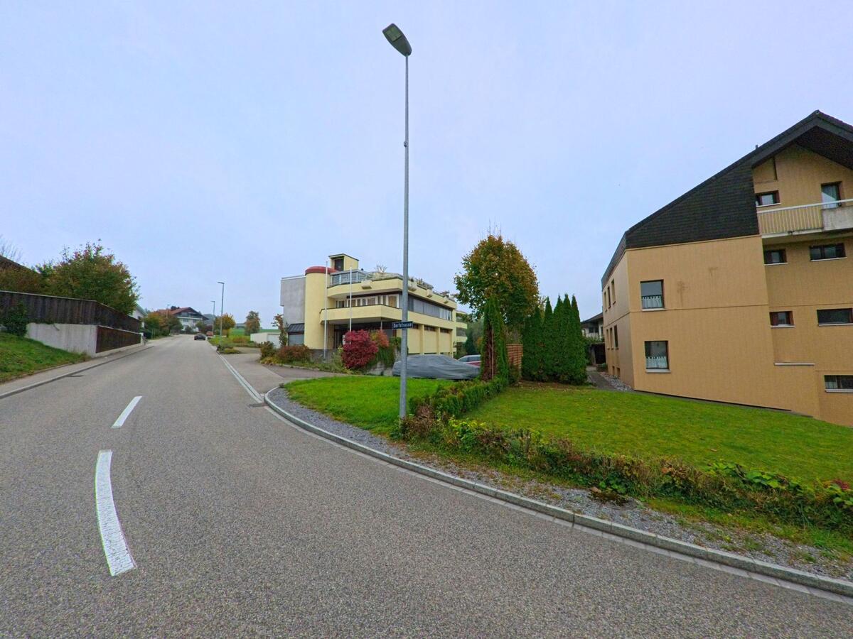 An einer leicht ansteigenden Strasse in Oberwil-Lieli (8966, Kanton Aargau) stehen moderne Mehrfamilienhäuser mit Balkonen und gepflegten Vorgärten.