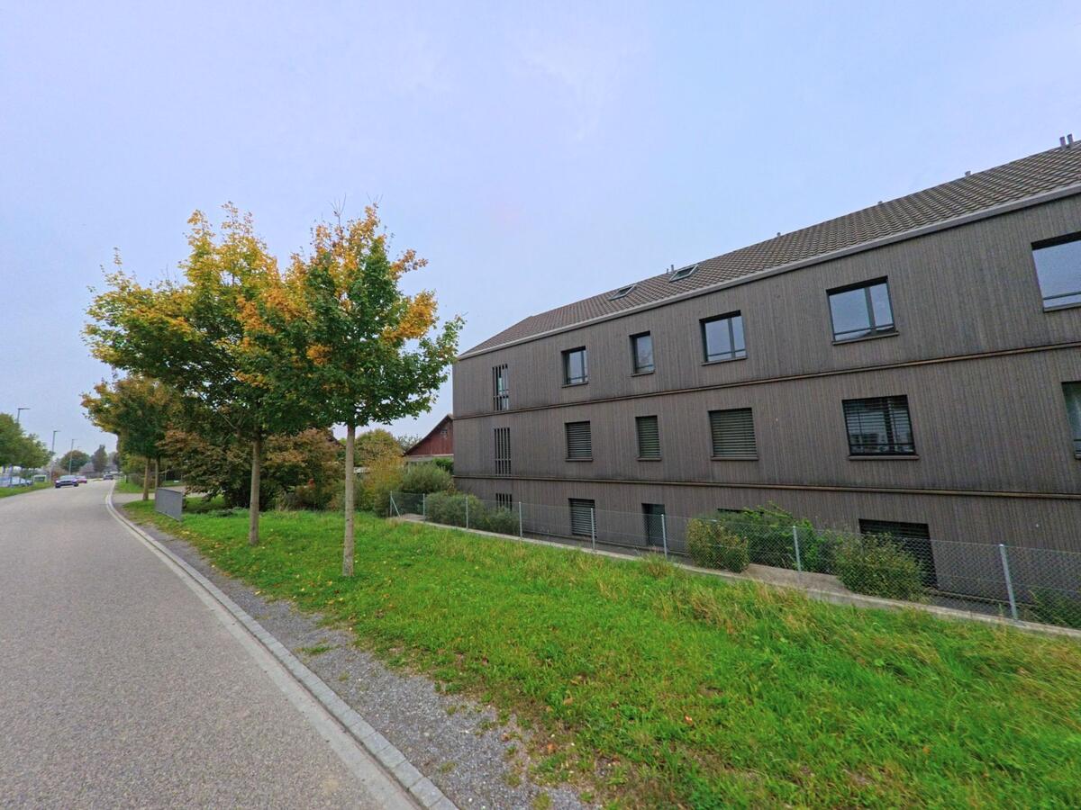 Ein modernes Wohnhaus mit Holzfassade steht an einer ruhigen Strasse in Oberwil-Lieli (8966, Kanton Aargau), gesäumt von jungen Bäumen mit herbstlichem Laub.