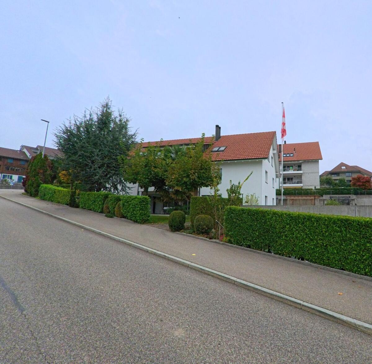 Ein gepflegtes Wohnhaus mit rotem Ziegeldach und einer Schweizer Fahne steht an einer ruhigen Strasse in Oberwil-Lieli (8966, Kanton Aargau).
