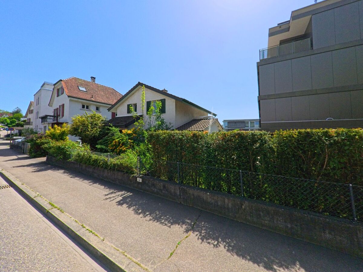 In Oberwil (4104 im Kanton Basel-Landschaft) stehen traditionelle Einfamilienhäuser mit Vorgärten neben modernen Neubauten entlang einer ruhigen Wohnstrasse.