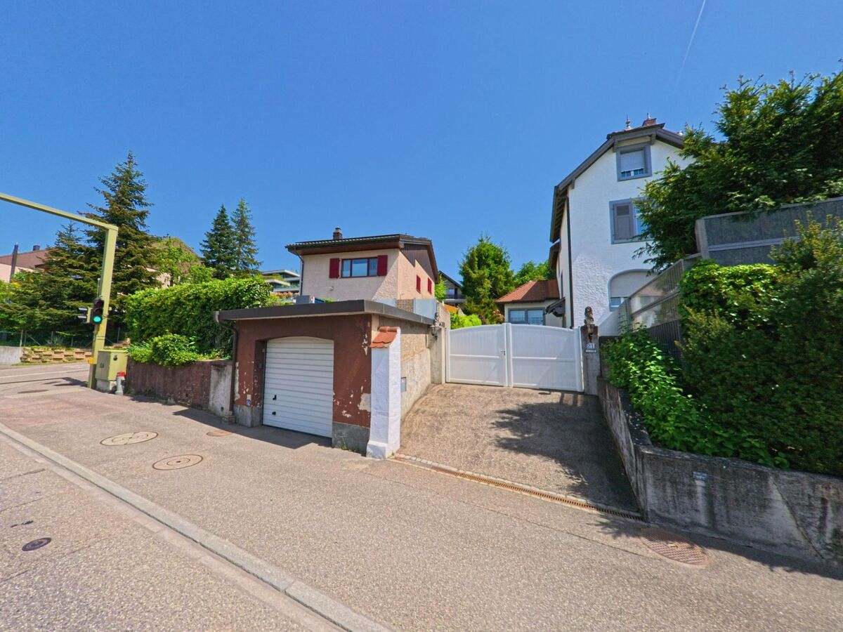 In Oberwil (PLZ 4104, Kanton Basel-Landschaft) führen Garagenzufahrten und Einfahrten zu Einfamilienhäusern entlang einer leicht ansteigenden Strasse mit Ampelanlage.