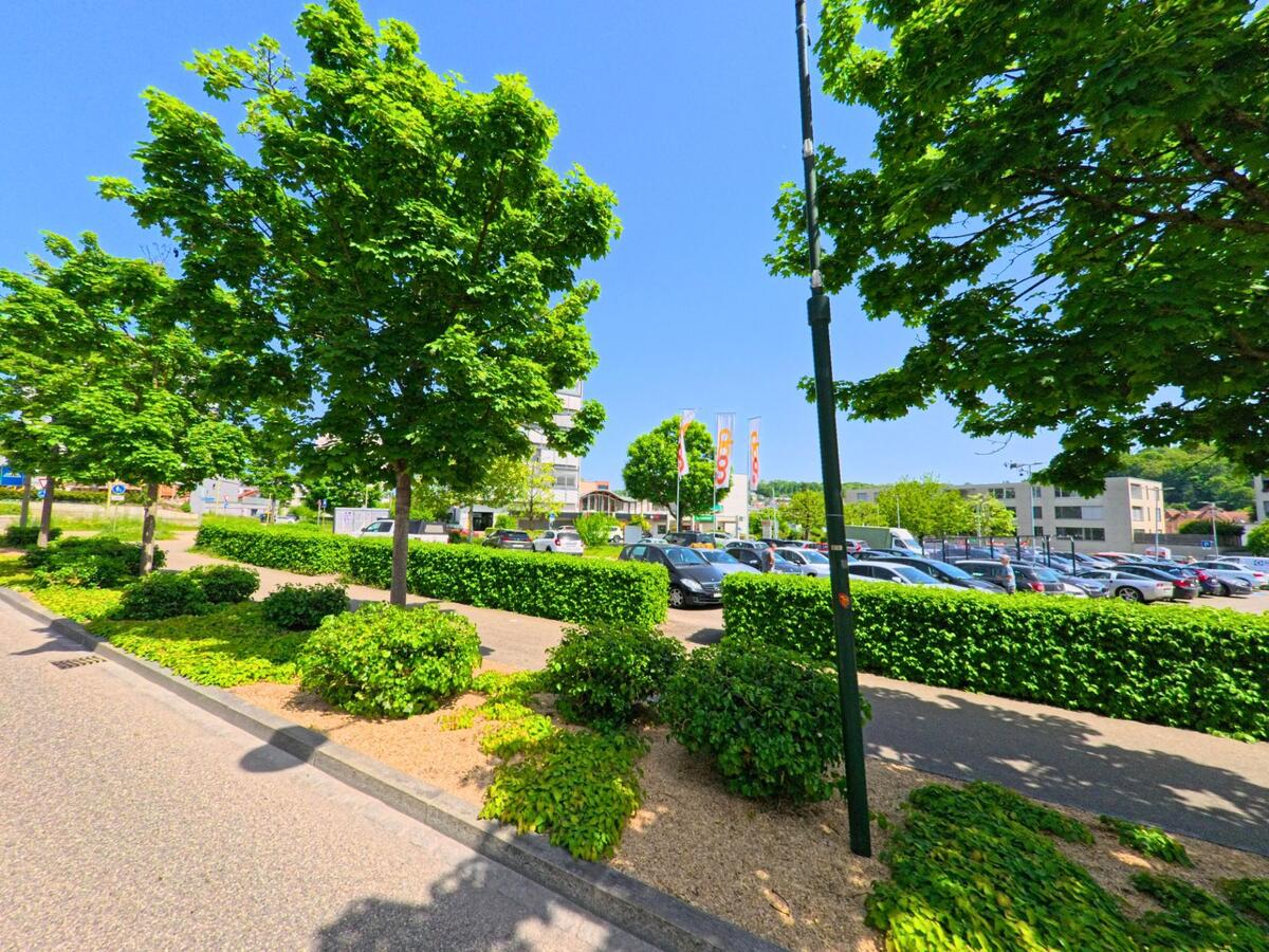 In Oberwil (PLZ 4104, Kanton Basel-Landschaft) erstreckt sich ein grosszügiger Parkplatz einer Einkaufszone, umgeben von Bäumen und gepflegten Hecken.