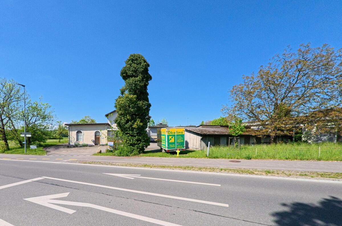 In Obfelden, PLZ 8912 im Kanton Zürich, steht ein Firmenanhänger mit Werbeaufschrift vor einem flachen Gewerbegebäude an einer mehrspurigen Strasse.