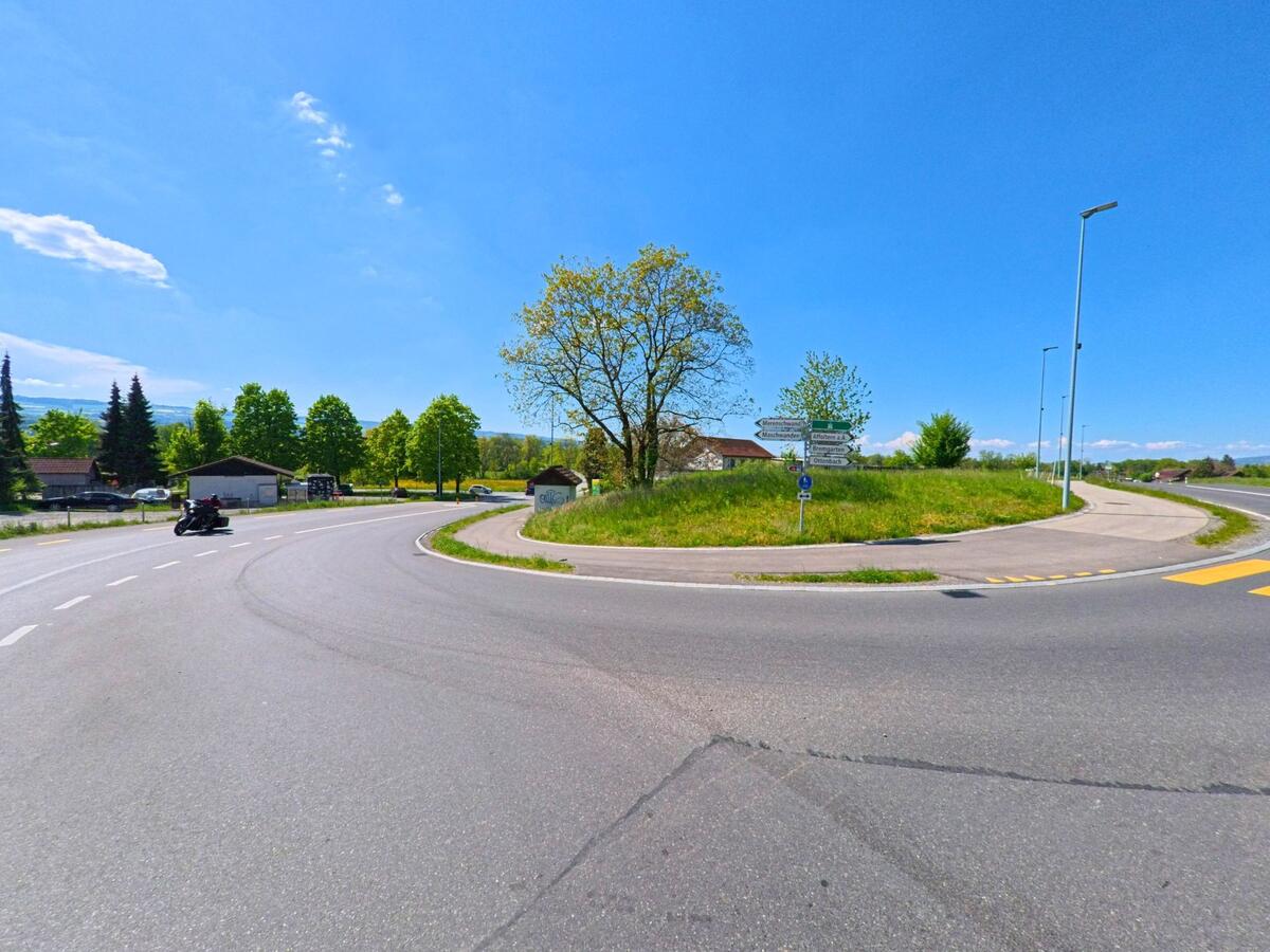 In Obfelden, PLZ 8912 im Kanton Zürich, treffen sich mehrere Strassen an einem übersichtlichen Verkehrsknotenpunkt mit Wegweisern und umliegendem Grünstreifen.