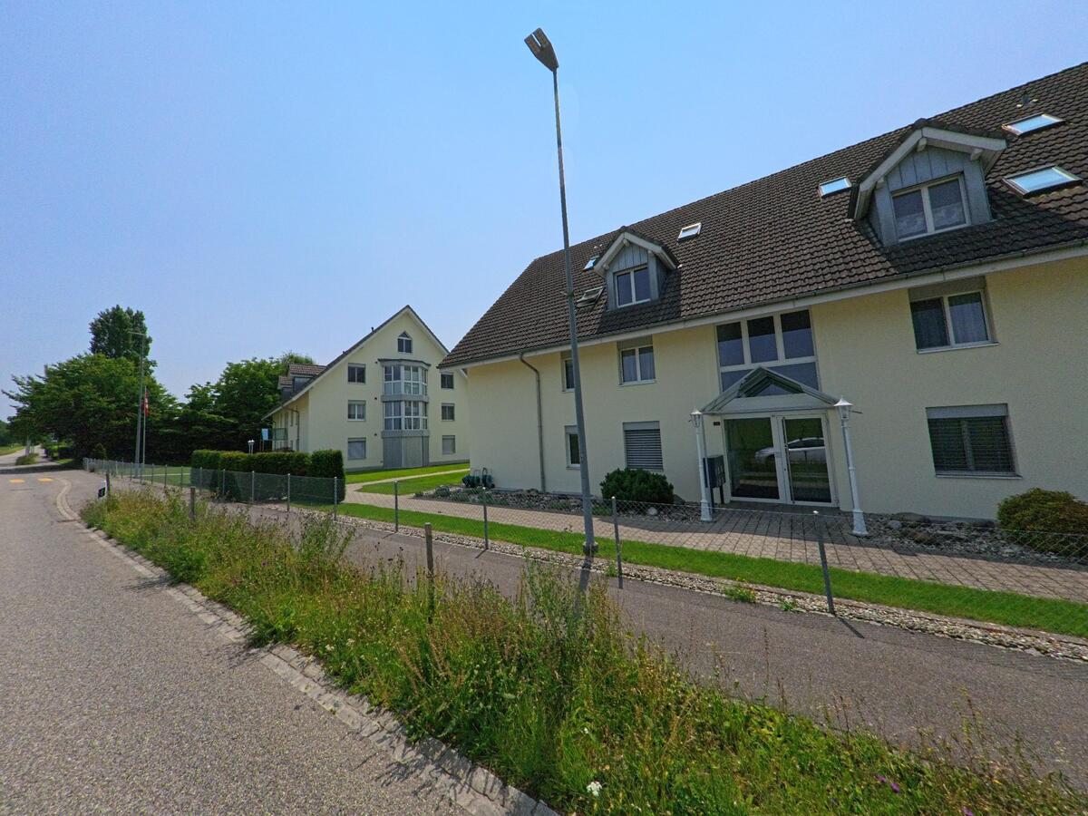 Entlang einer ruhigen Wohnstrasse in Oekingen (4566, Kanton Solothurn) stehen gepflegte Mehrfamilienhäuser mit grossen Dachgauben, begrünten Vorplätzen und eingezäuntem Gehweg..jpg
