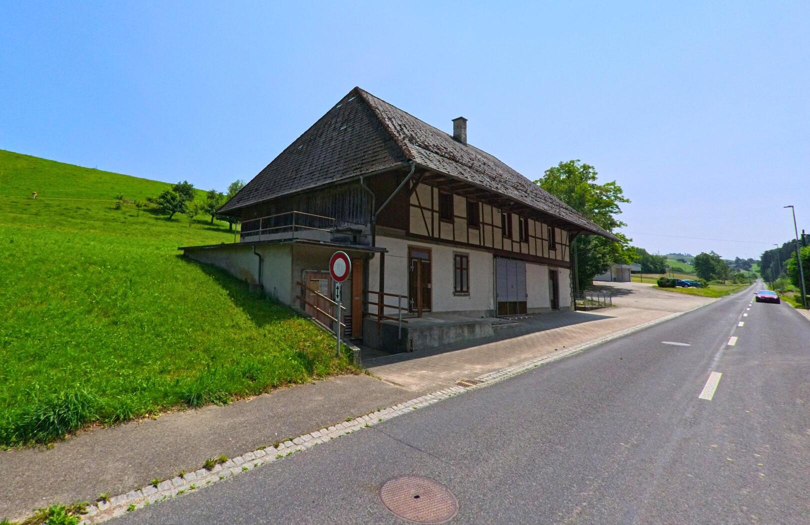 Ein traditionelles Gebäude mit Fachwerkfassade steht in Oeschenbach (4943, Kanton Bern) direkt an einer langen Landstrasse.