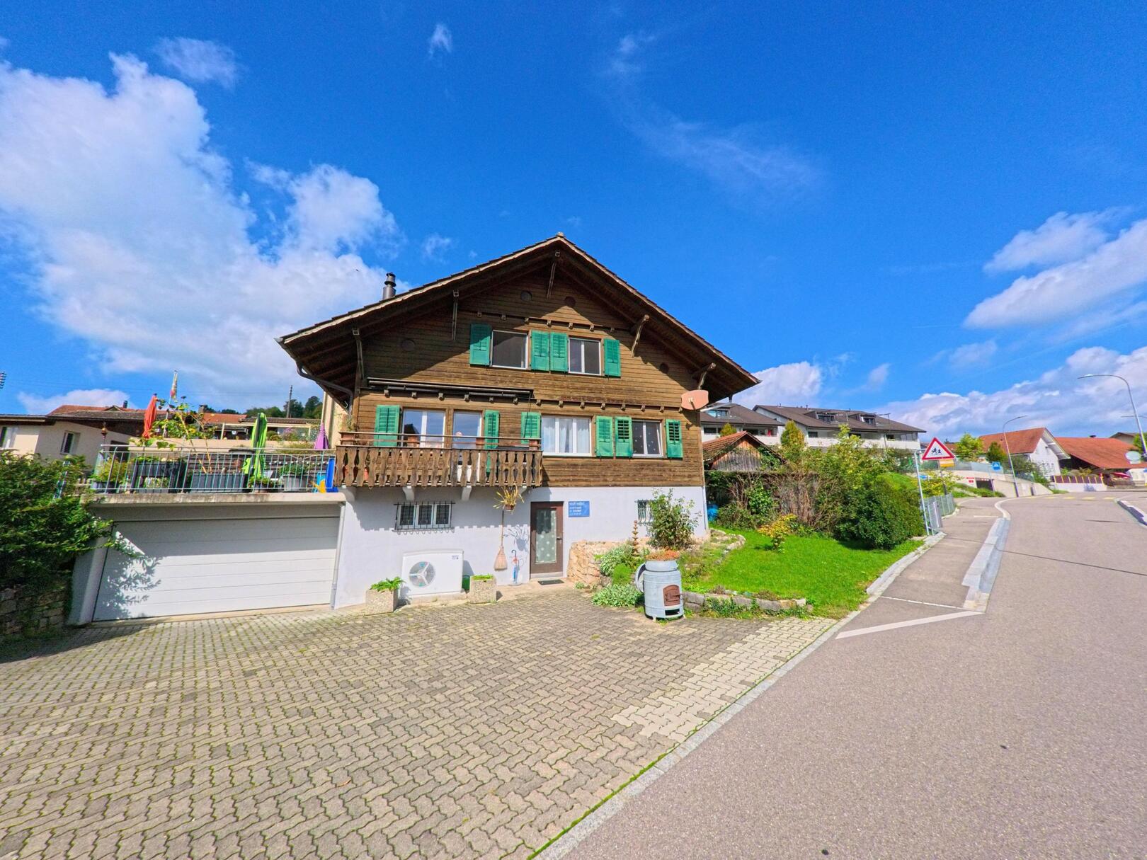 Ein traditionelles Haus mit Holzfassade und grünen Fensterläden steht an einer sonnigen Strasse in Oeschgen (5072, Kanton Aargau).