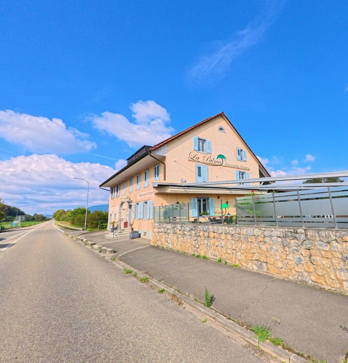 An der Hauptstrasse von Oeschgen (5072, Kanton Aargau) steht das Restaurant La Palma mit hellen Fassaden und blauen Fensterläden unter klarem Himmel.