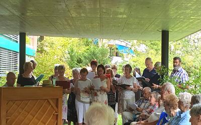 Beim Offenen Singen SoLei singt in Hofstetten-Flüh (4114, Kanton Solothurn) eine Gruppe gemeinsam vor einem sitzenden Publikum im Freien.
