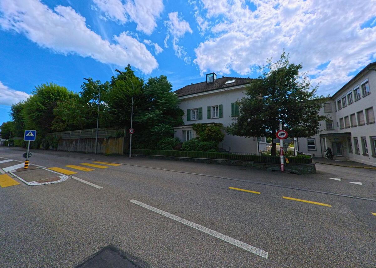 Ein traditionelles Wohnhaus mit gruenen Fensterlaeden steht in Oftringen (4665, Kanton Aargau) an einer Hauptstrasse mit Zebrastreifen und angrenzender Einbahnstrasse.