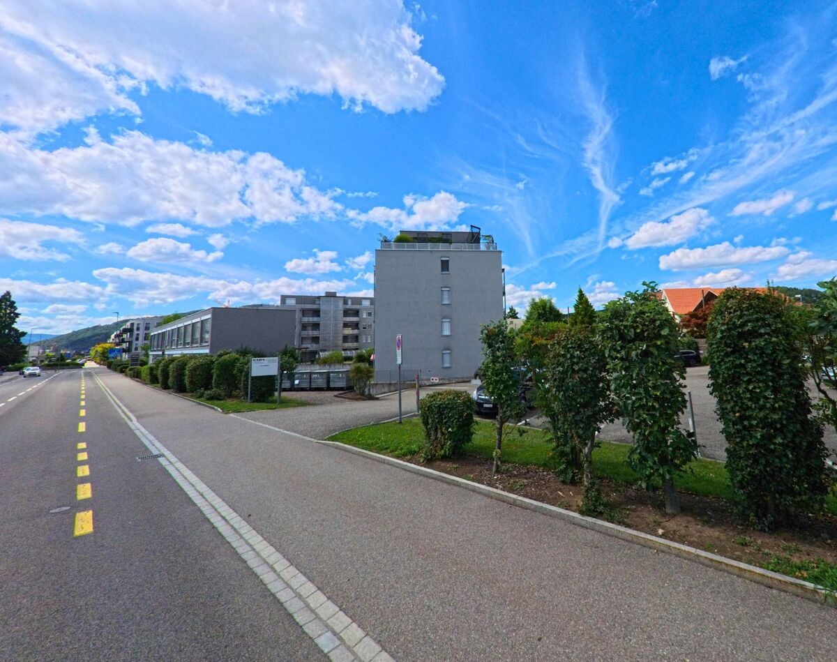 Entlang der grosszuegigen Hauptstrasse in Oftringen (4665, Kanton Aargau) befinden sich moderne Wohnbauten mit gepflegten Gruenanlagen und Parkplaetzen im Hintergrund.