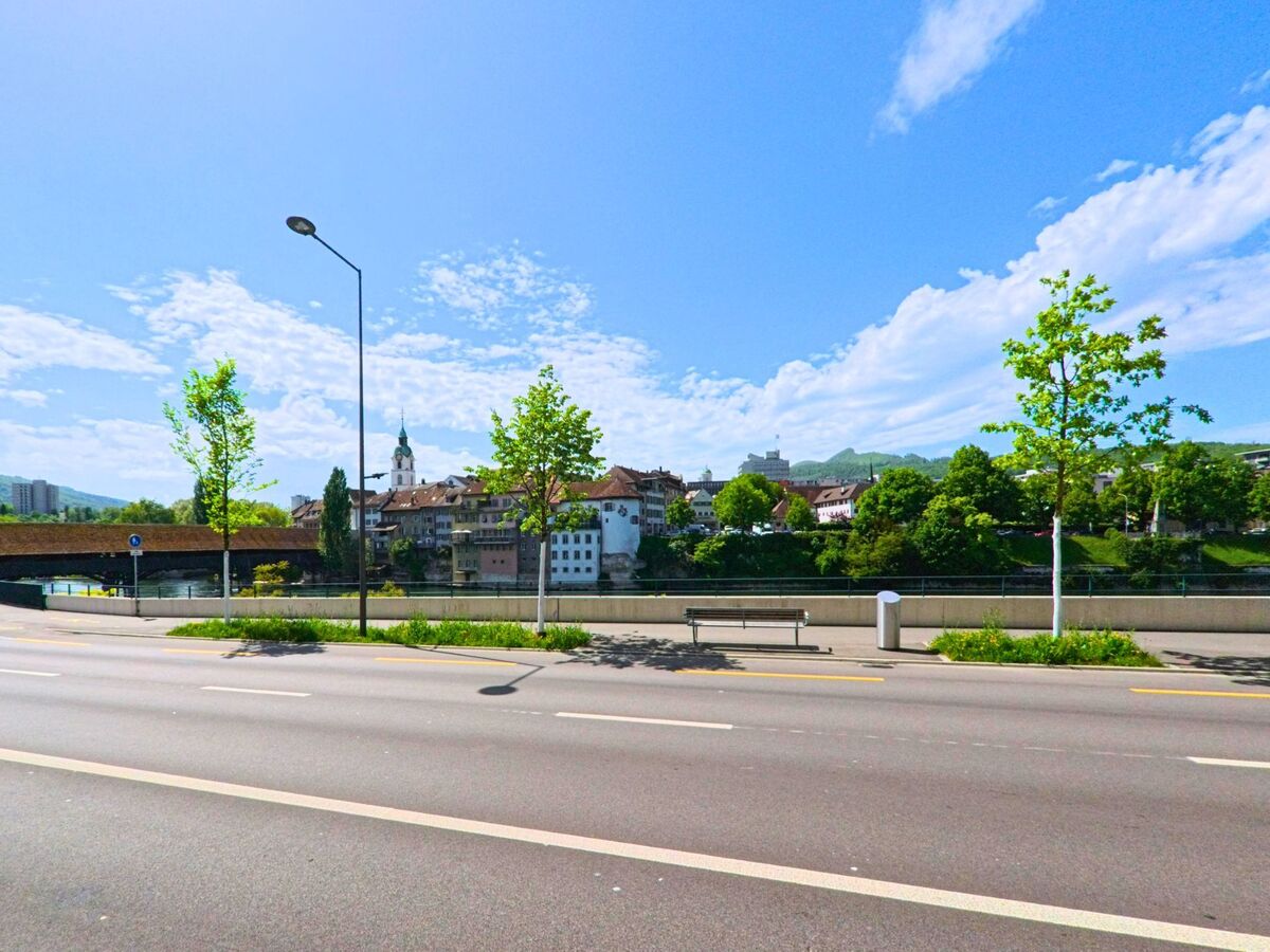 In Olten (4600, Kanton Solothurn) bietet eine breite Strasse mit Mittelinsel Ausblick auf die historische Altstadt und die gedeckte Holzbruecke ueber die Aare.