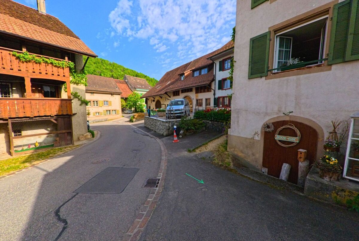 In einer engen Gasse von Oltingen (4494, Kanton Baselland) reihen sich historische Wohnhäuser mit Holzbalkonen und Fensterläden aneinander.