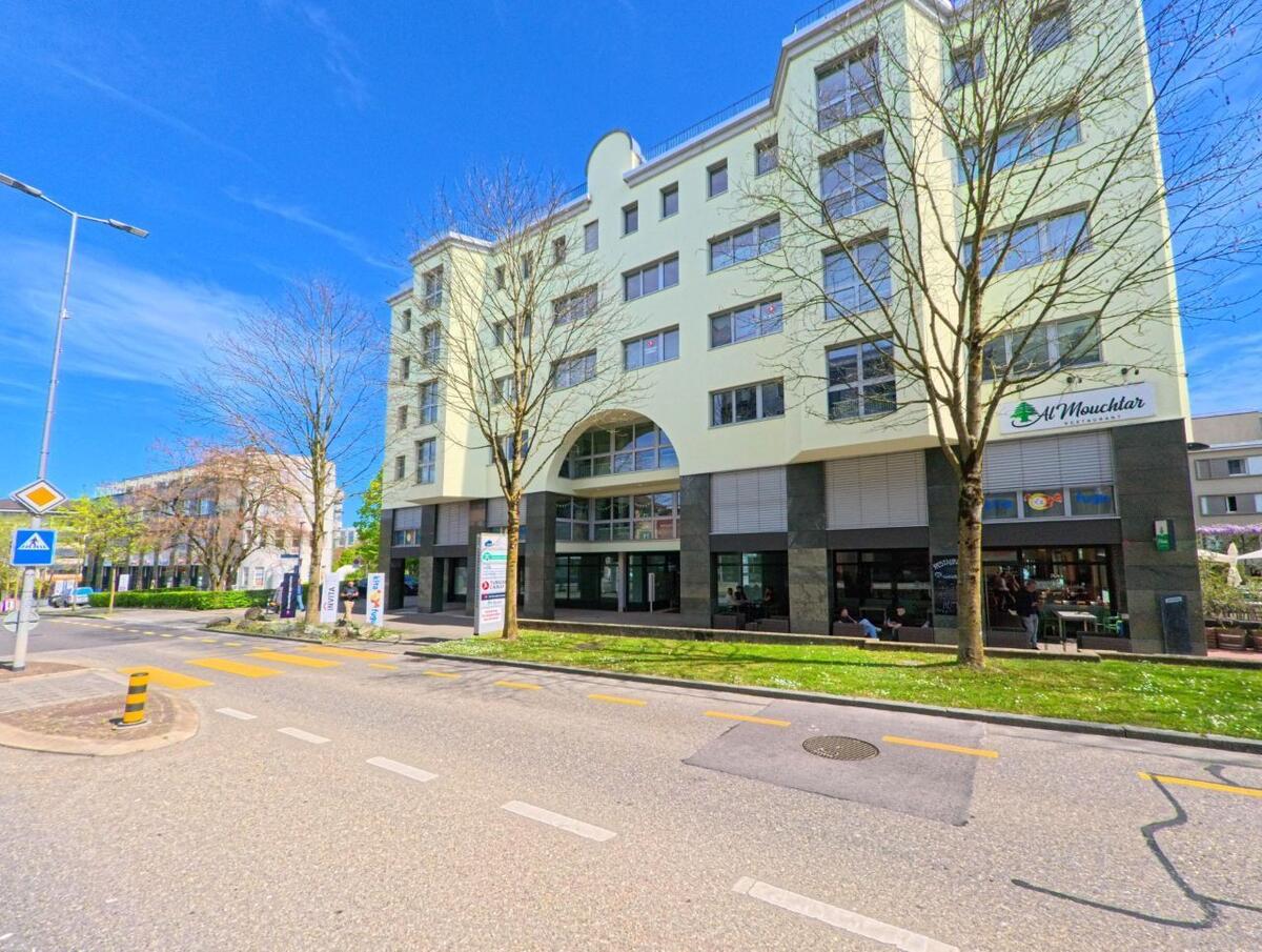 Ein mehrstöckiges Gebaeude mit Gastronomiebetrieb im Erdgeschoss steht in Opfikon (8152, Kanton Zürich) an einer Strasse mit Fussgaengerueberweg.