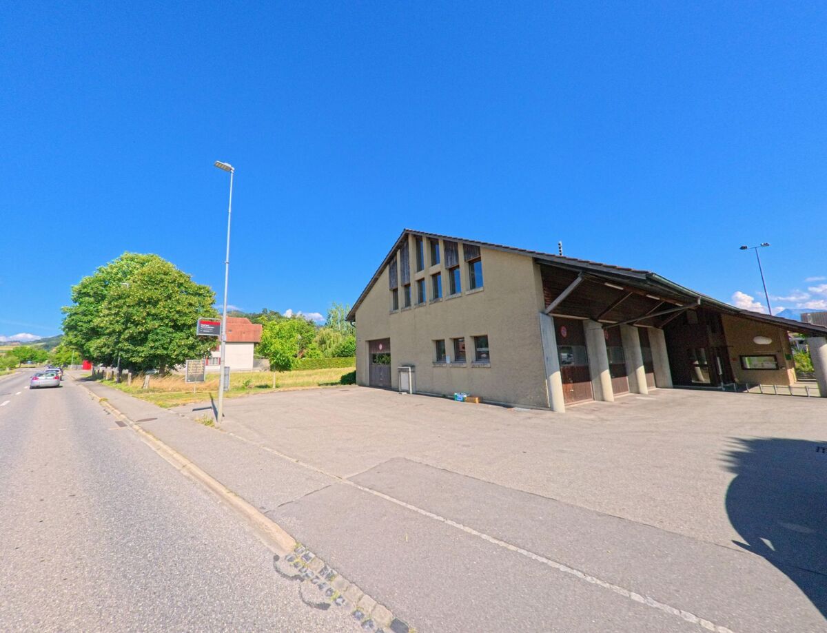 In Oppligen (3629, Kanton Bern) befindet sich ein schlichtes Feuerwehrgebäude mit mehreren Toren an einer breiten Strasse, neben einer Bushaltestelle und umgeben von Wiesen.