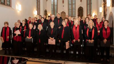 In einer Kirche steht in Liestal (4410, Kanton Baselland) der Oratorienchor in schwarzer Kleidung mit roten Schals gemeinsam zu einem Gruppenfoto auf der Bühne.