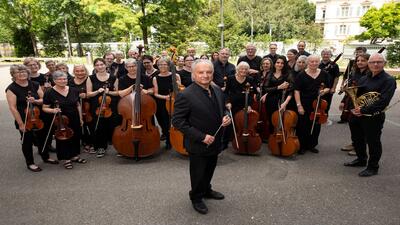 Der Orchesterverein steht mit Streich- und Blasinstrumenten hinter seinem Dirigenten zu einem Gruppenbild in Aarau (5000, Kanton Aargau).