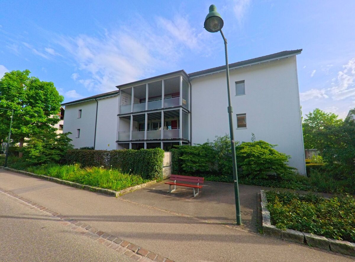 In Ormalingen (PLZ 4466, Kanton Baselland) steht ein modernes Mehrfamilienhaus mit Balkonen hinter einer gepflegten Grünfläche mit Sitzbank am Gehweg.