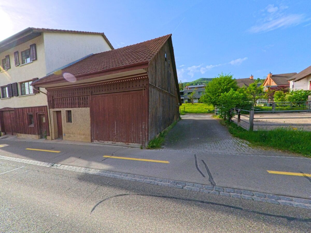  In Ormalingen (PLZ 4466, Kanton Baselland) führt ein gepflasterter Weg zwischen einer alten Scheune und einer Pferdekoppel in ein Wohnquartier mit Einfamilienhäusern.