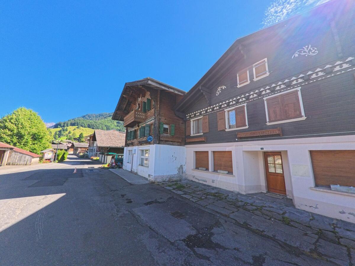 Entlang einer Dorfstrasse in Ormont-Dessous (1866, Kanton Waadt) reihen sich traditionelle Holzhäuser vor den grünen Hängen.