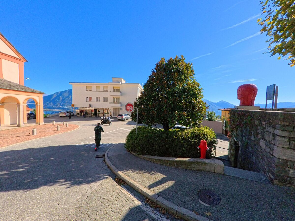 Am Platz bei der Kirche in Orselina (6644, Kanton Tessin) treffen sich Spaziergänger und Fahrzeuge mit Aussicht auf den Lago Maggiore.