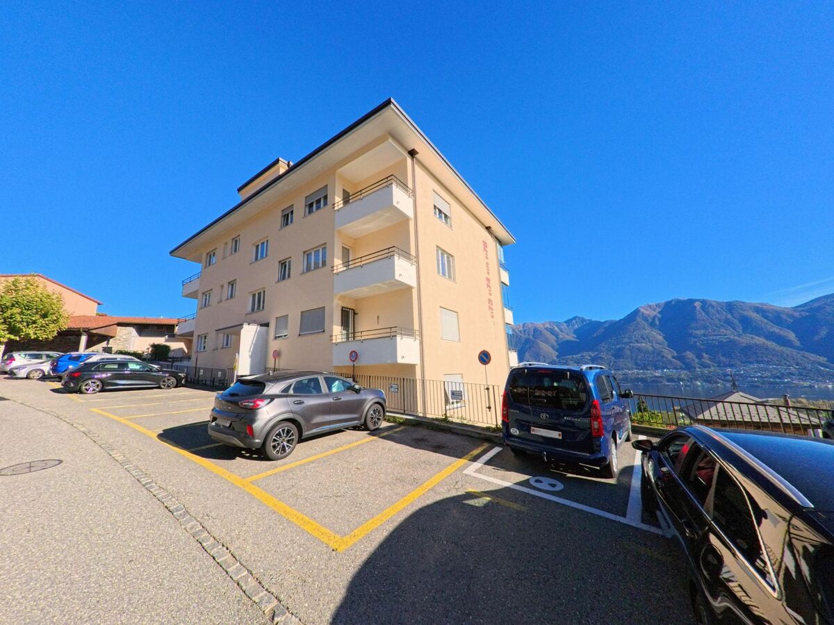 Ein helles Mehrfamilienhaus mit Balkonen steht in Orselina (6644, Kanton Tessin) oberhalb von Parkplätzen mit Blick auf den Lago Maggiore.