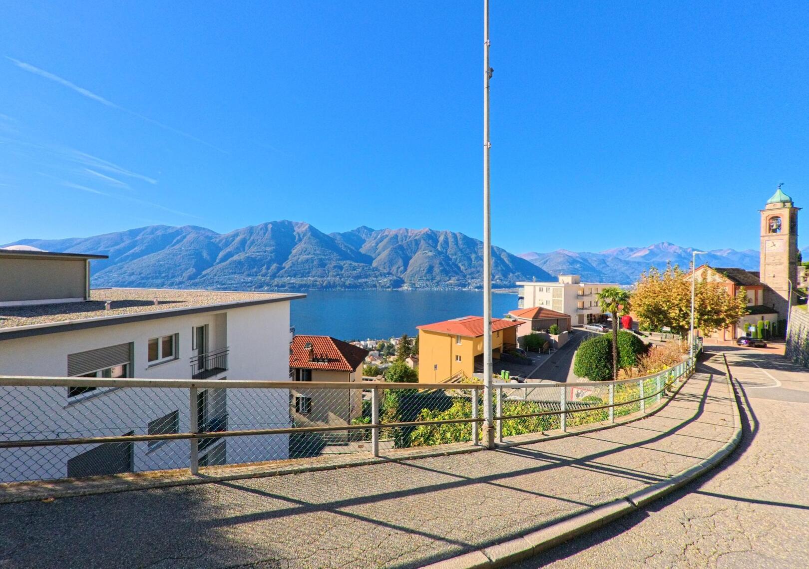 Eine abfallende Strasse in Orselina (6644, Kanton Tessin) führt an der Kirche vorbei und bietet einen weiten Blick über den Lago Maggiore.
