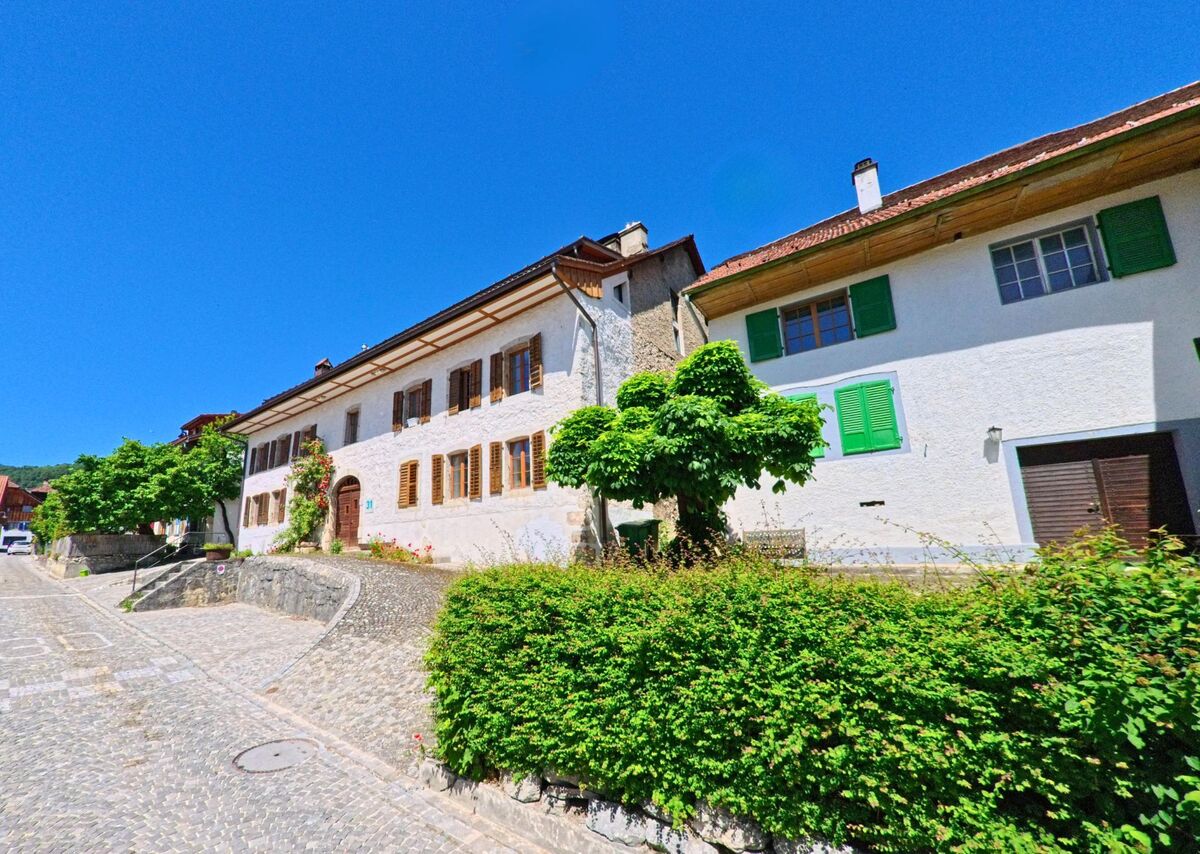 In Orvin (2534, Kanton Bern) erstrecken sich gepflegte Häuser mit Fensterläden entlang einer ansteigenden Pflasterstraße, gesäumt von Büschen und kleinen Bäumen.