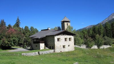 Das Ospiz Chapella in Cinuos-chel (7526, Kanton Graubuenden) ist ein historisches Steingebaeude mit Turm, umgeben von Wald und Bergen.