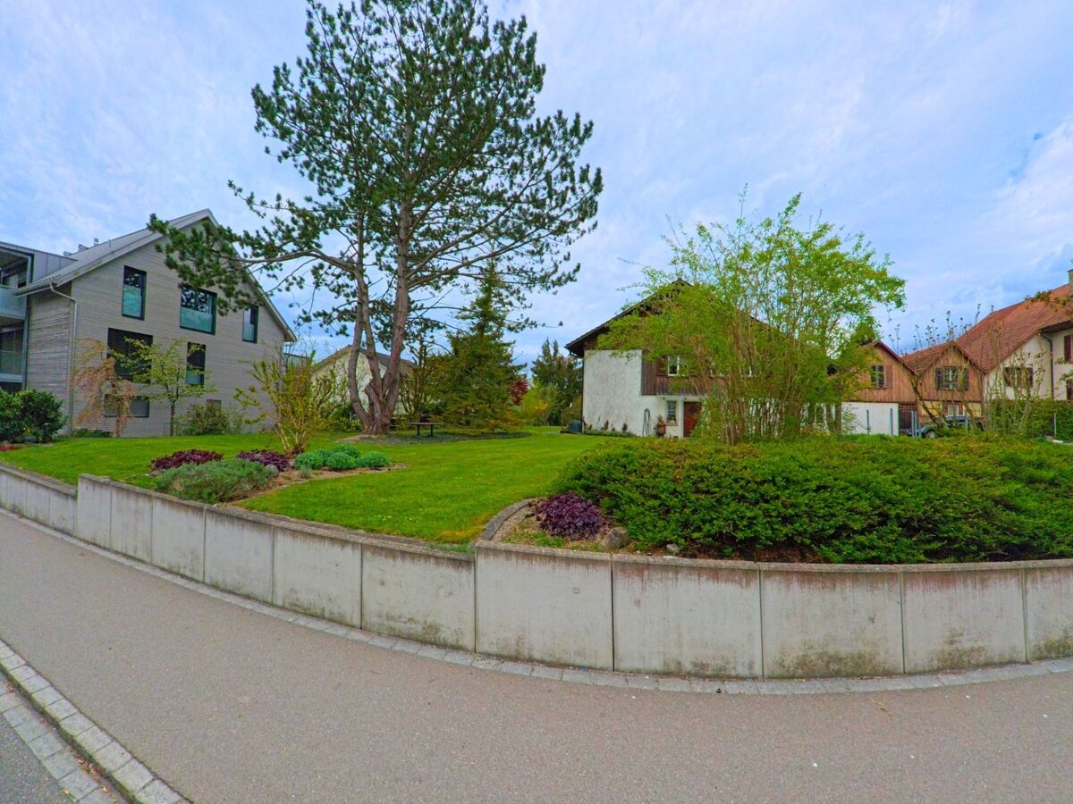 In Ossingen, PLZ 8475 im Kanton Zürich, erstreckt sich eine gepflegte Grünanlage mit Bäumen und Sträuchern zwischen Wohnhäusern unterschiedlicher Bauart.