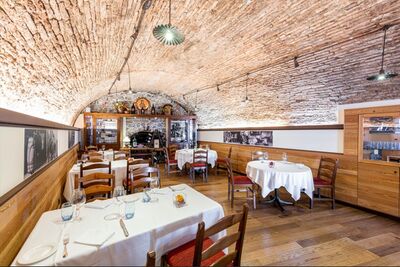 In der Osteria Lanterna in Mendrisio (6850, Kanton Tessin) steht ein gemuetlicher Speiseraum mit gewoelbter Backsteinwand und gedeckten Tischen.