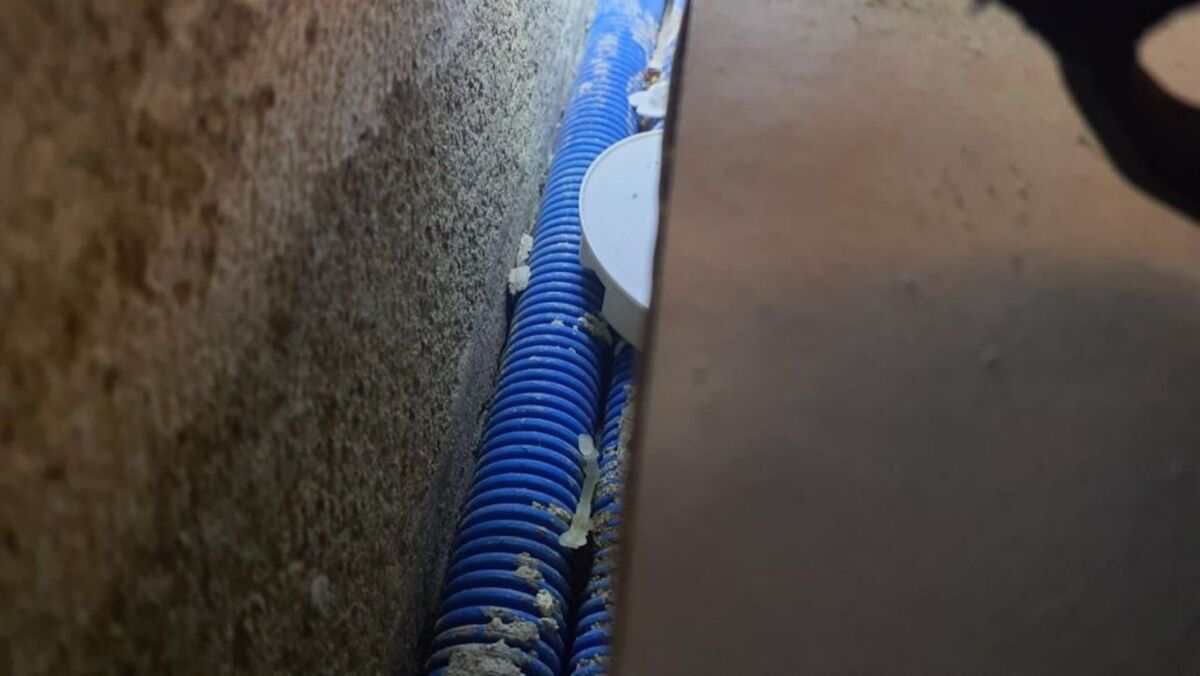  In einem Zwischenraum eines Gebäudes in Otelfingen (8112, Kanton Zürich) verlaufen blaue Kabelschutzrohre dicht an einer Betonwand entlang, umgeben von Bauschmutz und Isolierresten.