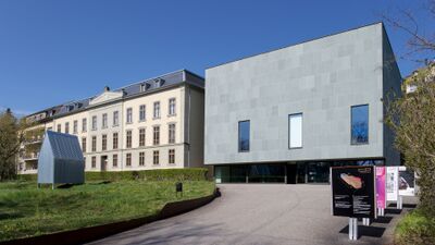 In Biel/Bienne (2502, Kanton Bern) steht das Pasquart, ein modernes Gebaeude aus grauen Steinplatten neben einem historischen Bau mit klassischer Fassade unter blauem Himmel.